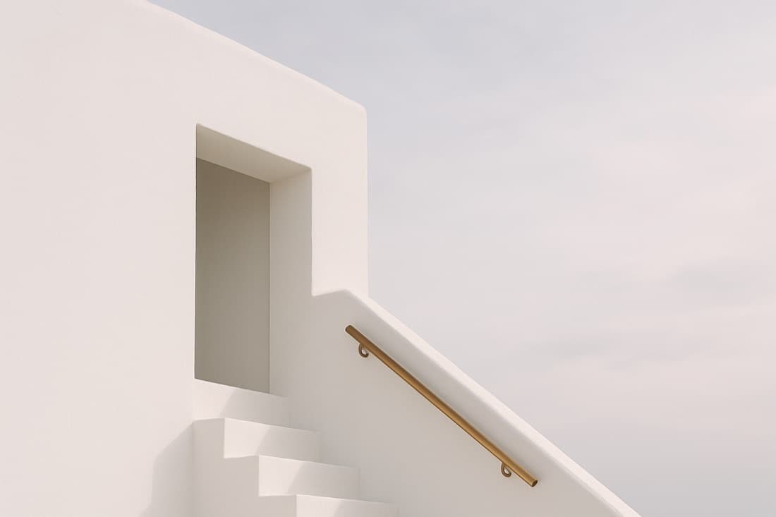 A white stucco stair with a brass handrail against a pale coastal sky