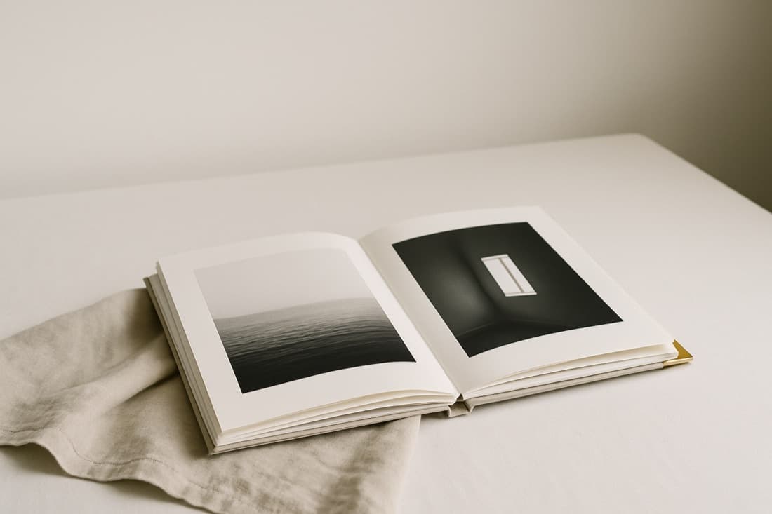 An open photography monograph on a linen surface, two minimalist plates showing